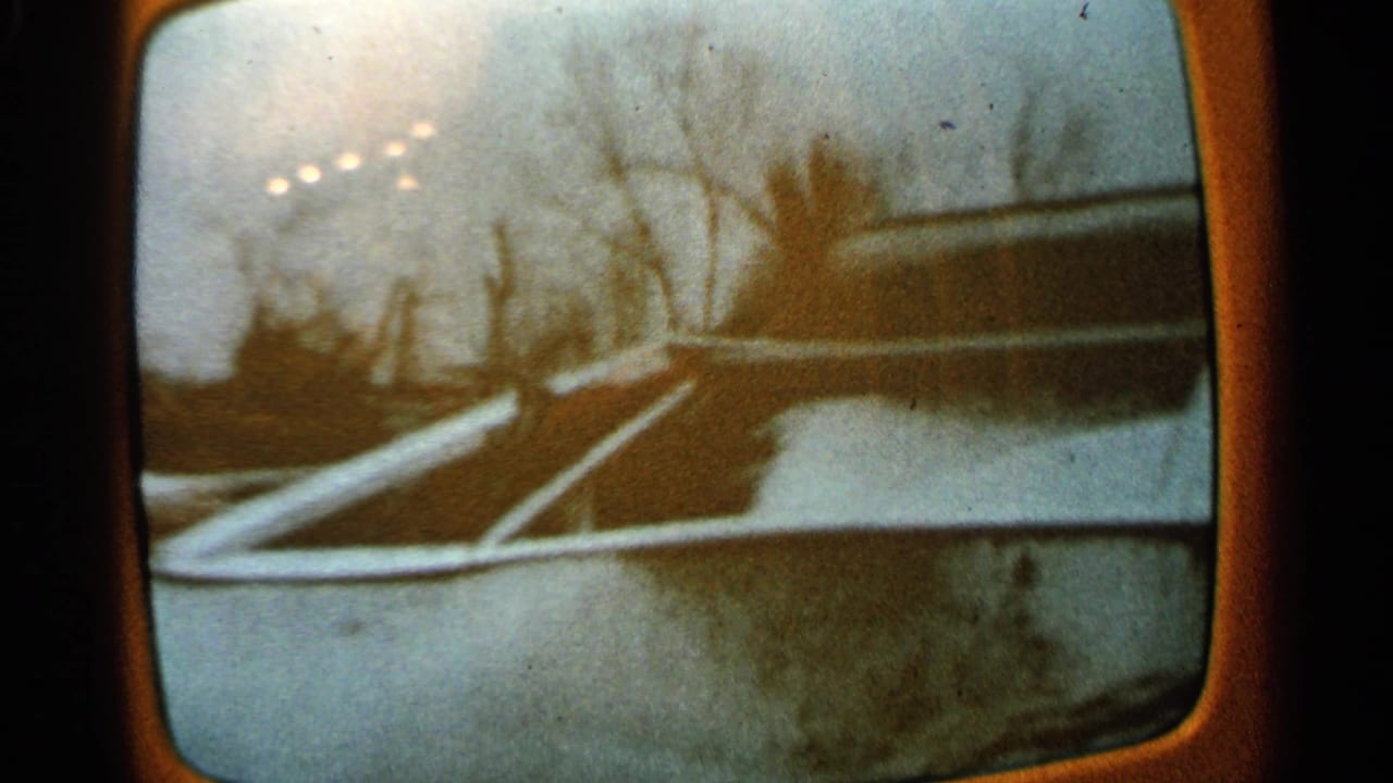 1965 Minnesota home-movie frame looking through a vehicle window at snow, bare trees, and small distant lights.