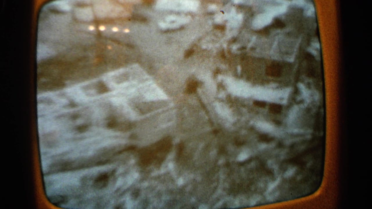 Television screen with blurred aerial view of flooded buildings and pale water areas.