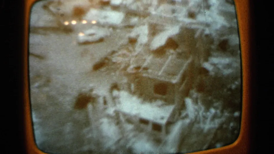 Home-movie shot of a TV broadcast showing an aerial flood scene with damaged buildings, water, and debris-like forms.