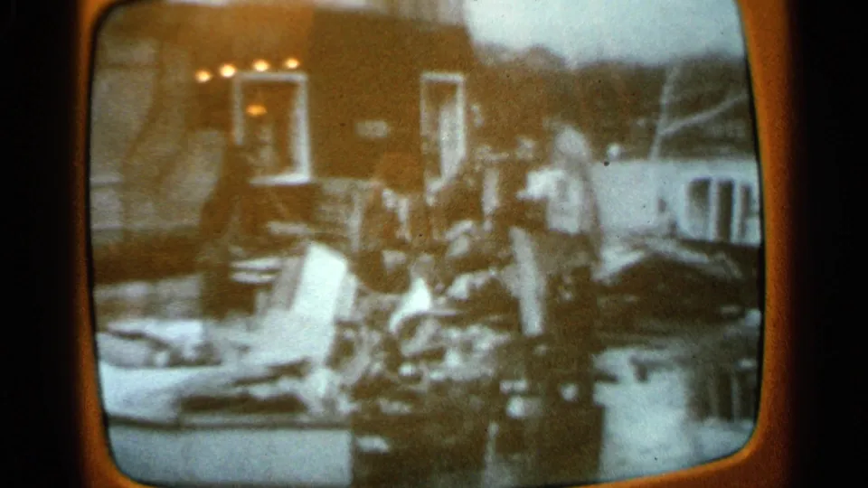1965 Minnesota home-movie capture of TV tornado cleanup coverage, with people visible among debris near a damaged structure.