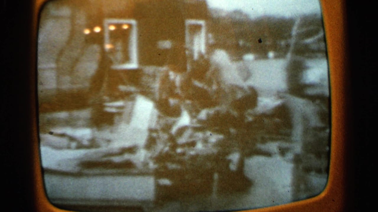 1965 Minnesota 8mm frame of a rounded television screen showing grainy black-and-white footage with people amid debris.