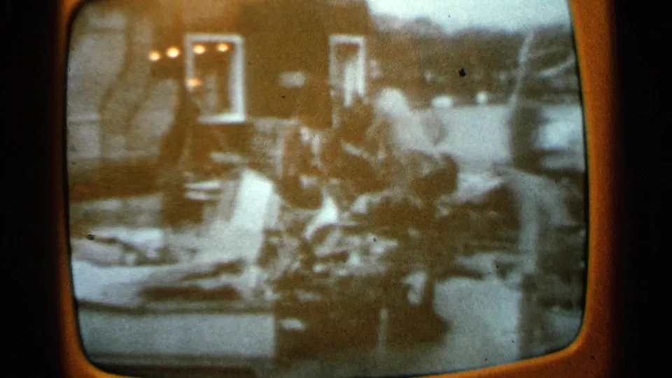 1965 Minnesota 8mm frame of a rounded television screen showing grainy black-and-white footage with people amid debris.