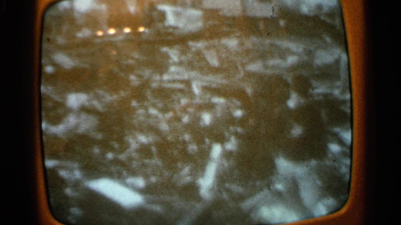 Television screen showing a person near debris and damaged outdoor ground.