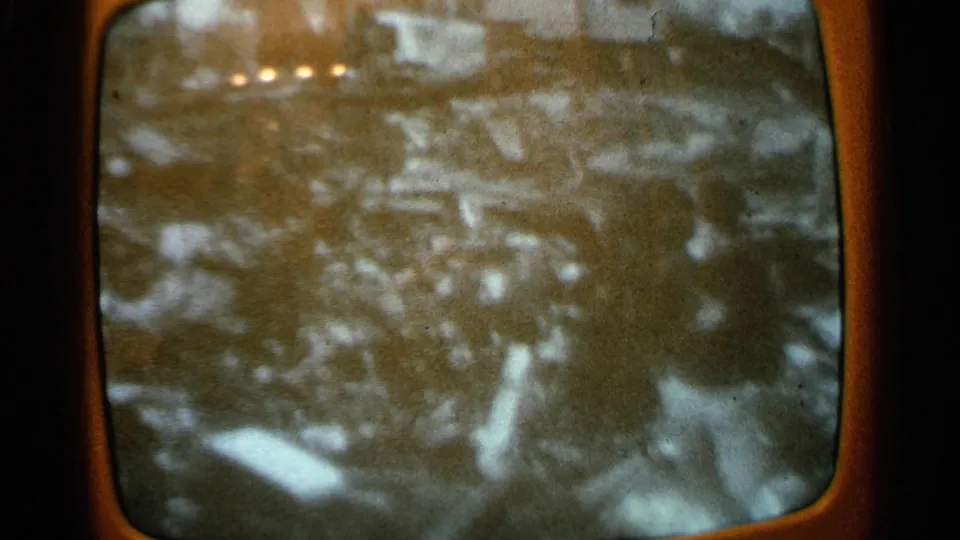 1965 Minnesota home-movie frame of a TV screen with black-and-white footage of a person standing near scattered debris.
