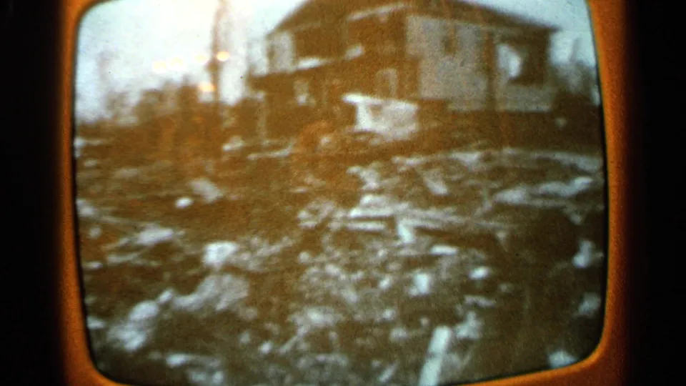 1965 Minnesota 8mm still of a rounded TV screen showing black-and-white footage of a house and debris-strewn ground.