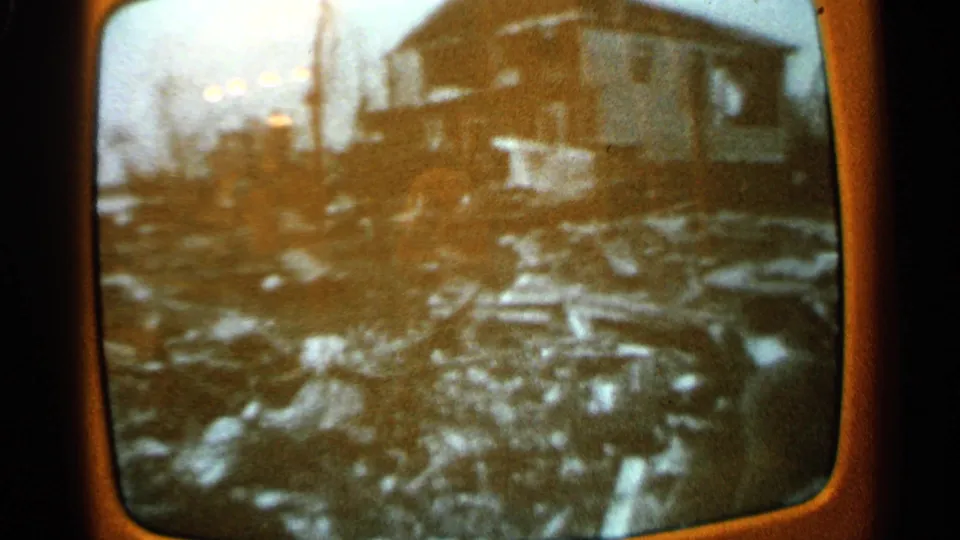 1965 Minnesota home-movie frame of a television screen showing a house and debris in soft black-and-white broadcast footage.