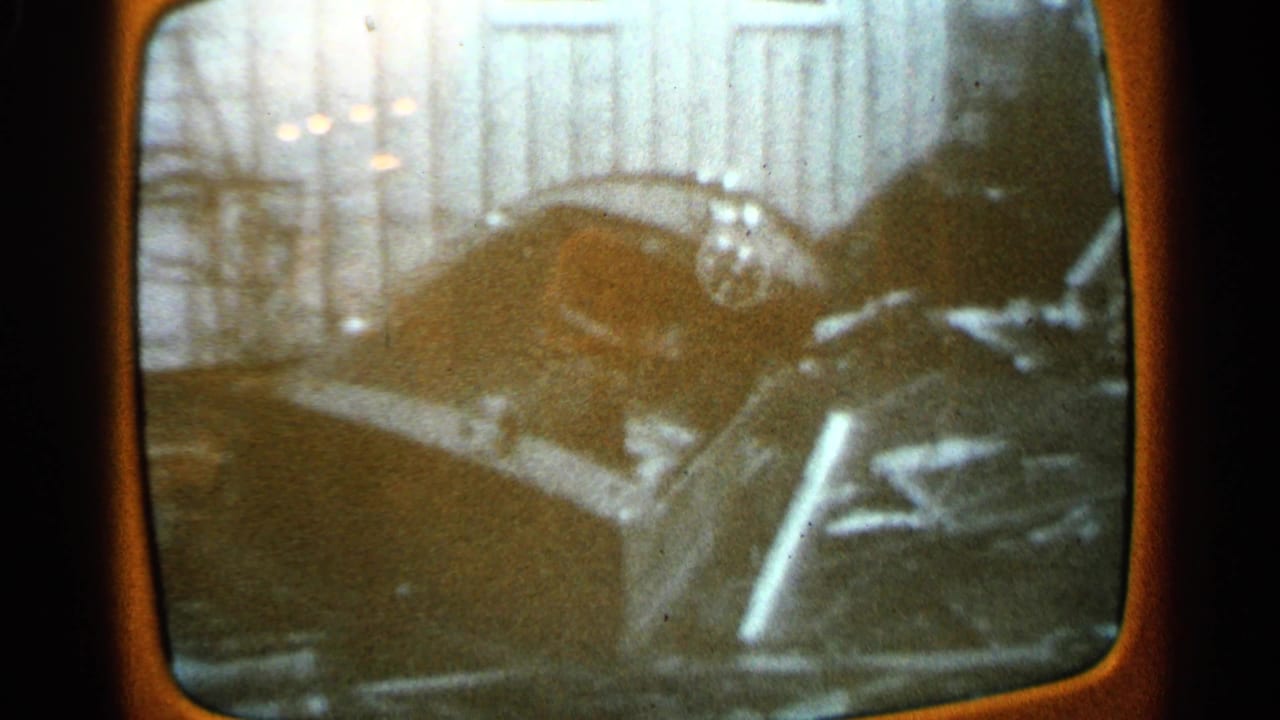 1965 Minnesota television footage re-filmed on 8mm showing a crushed car amid structural storm damage.