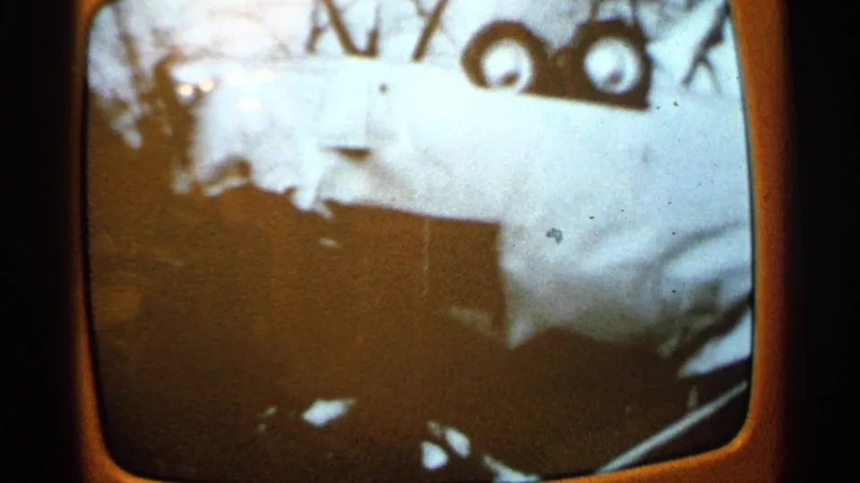 1965 Minnesota storm aftermath footage on a TV screen showing pale wreckage, debris, and dark foreground shapes.