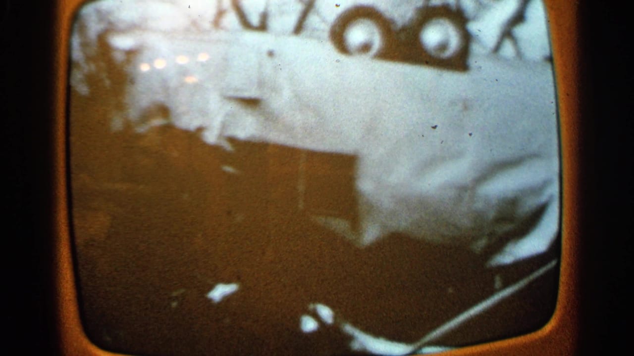 1965 Minnesota 8mm frame of an orange television screen showing a damaged white vehicle or large body panel surrounded by debris.