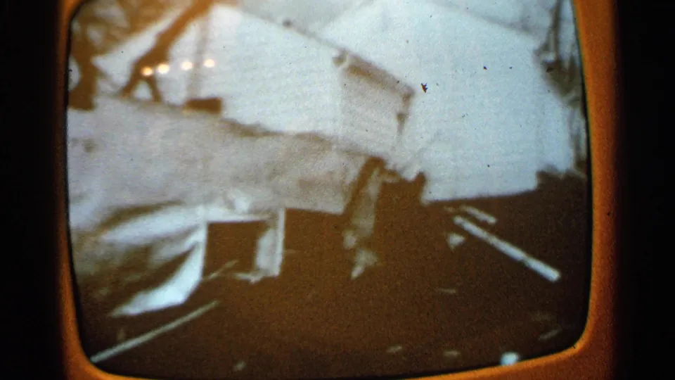 1960s home-movie frame of a tilted television image showing damaged white material, dark debris, and broadcast flicker.