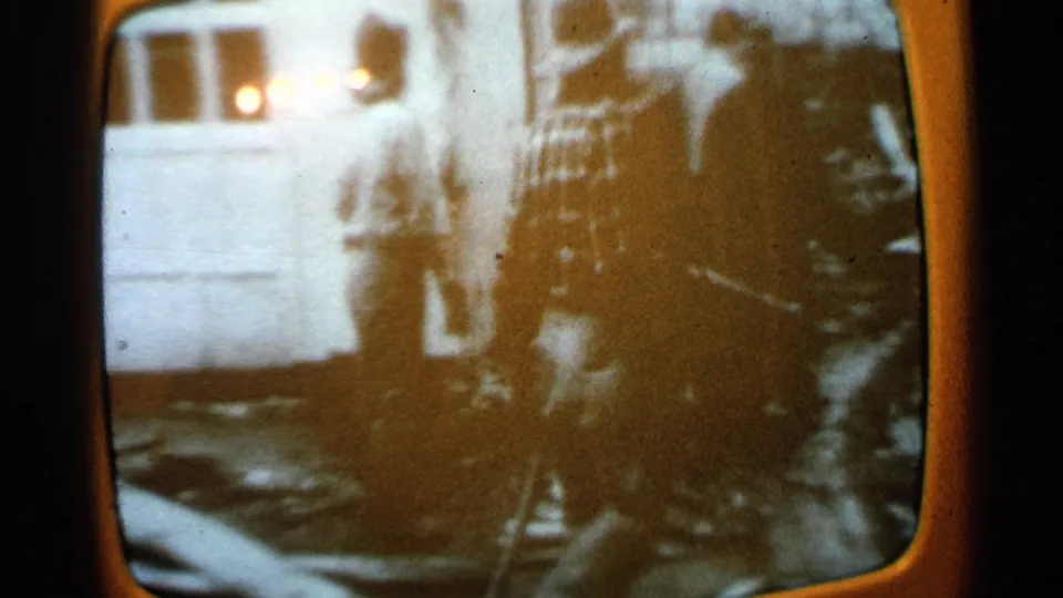 1965 Minnesota home-movie frame showing a person near a residential exterior, with debris and equipment in the foreground.