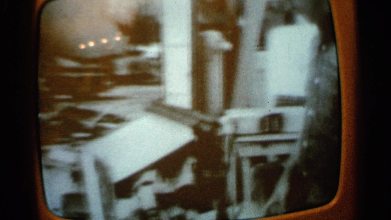 1965 Minnesota 8mm footage viewed through a television screen, showing a man near a parked car and scattered outdoor objects.