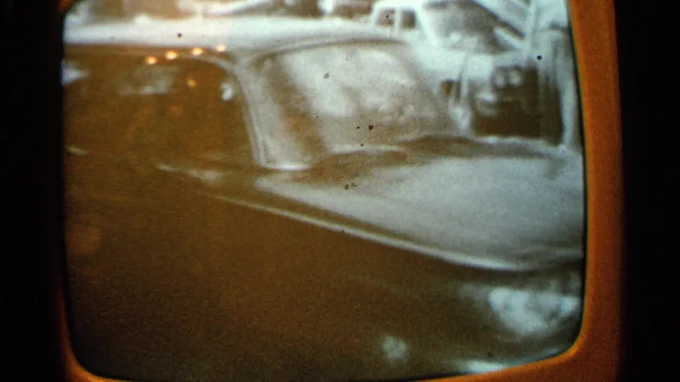 A closer 8mm view shows the parked car's windshield and body, with television-screen curvature and film grain visible.