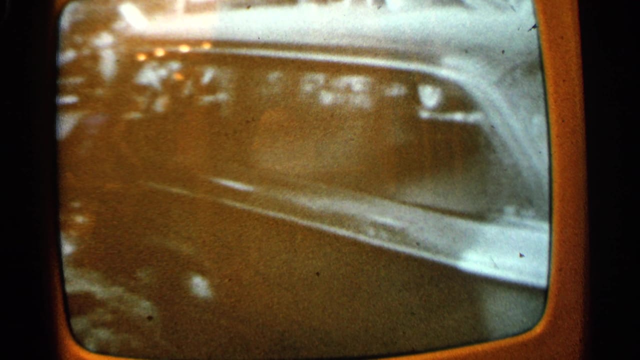 1965 Minnesota 8mm frame of an orange vintage television showing a blurred broadcast view of damage and wreckage.