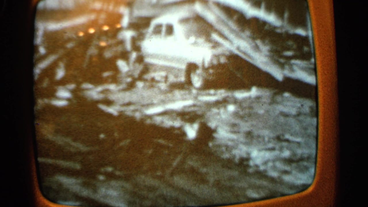 Television broadcast showing a light-colored car among debris.