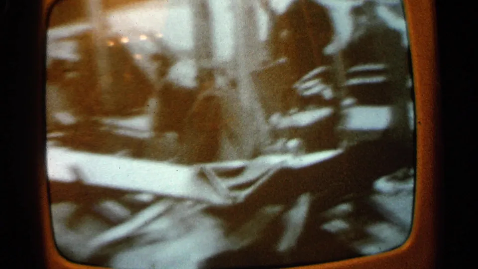 1965 Minnesota home-movie frame of a television screen showing blurred figures near wreckage and debris after damage.