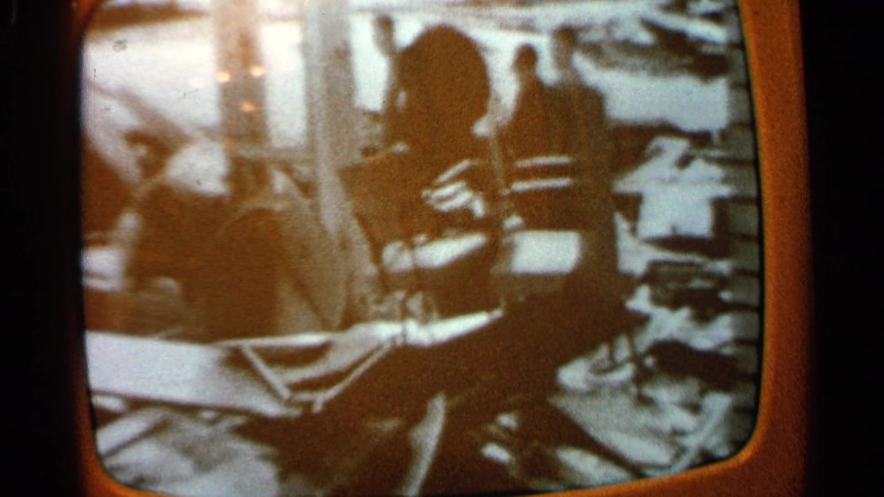 Blurred screen-like view with indistinct figures and room details in warm, faded film color.