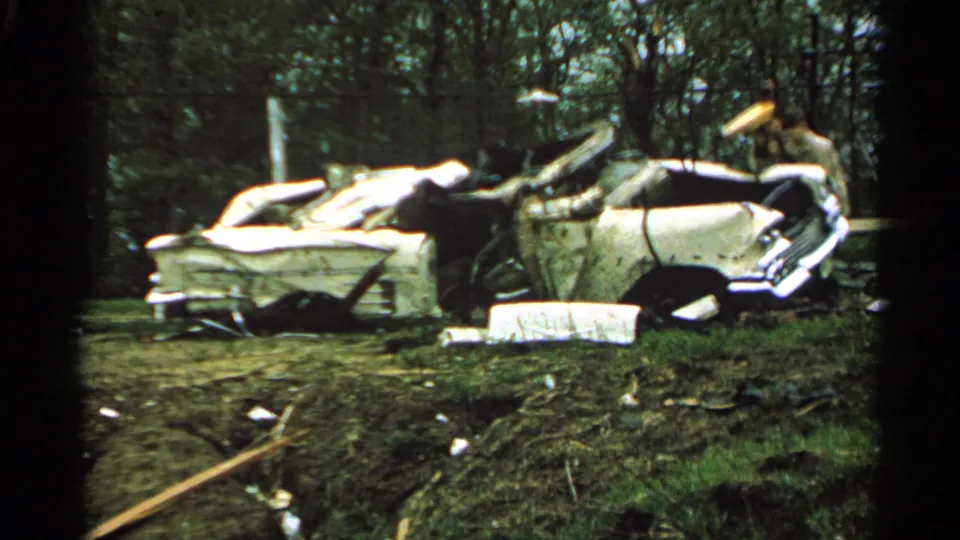 1965 Minnesota 8mm frame showing a crushed white car with its roof collapsed amid scattered storm debris.