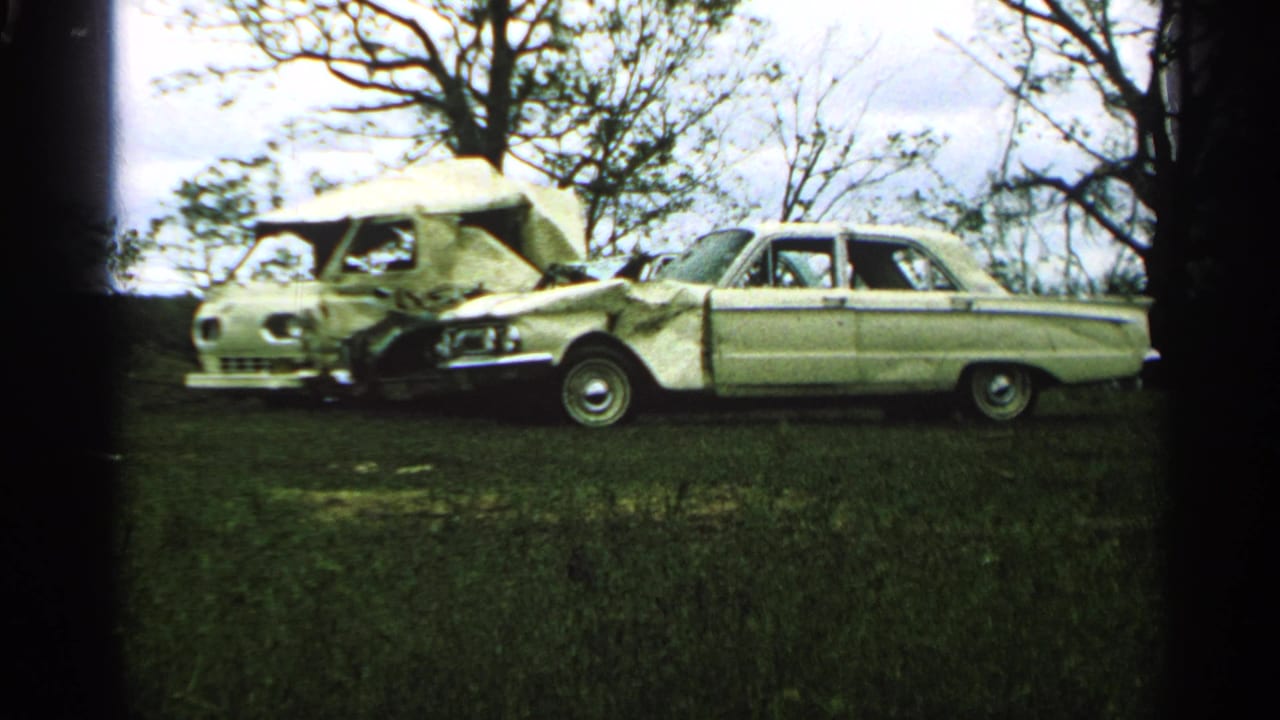 Damaged sedan beside a crushed camper van in a grassy field.