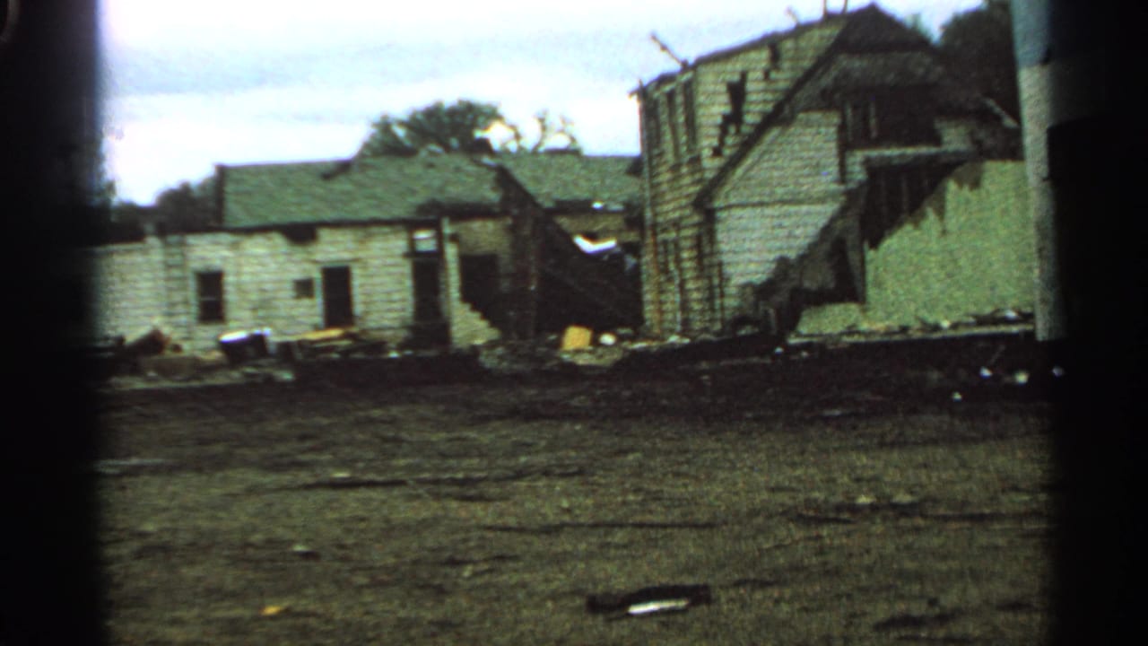 Minnesota 1965 frame showing a wrecked residential structure with broken siding, open wall areas, and debris across the yard.