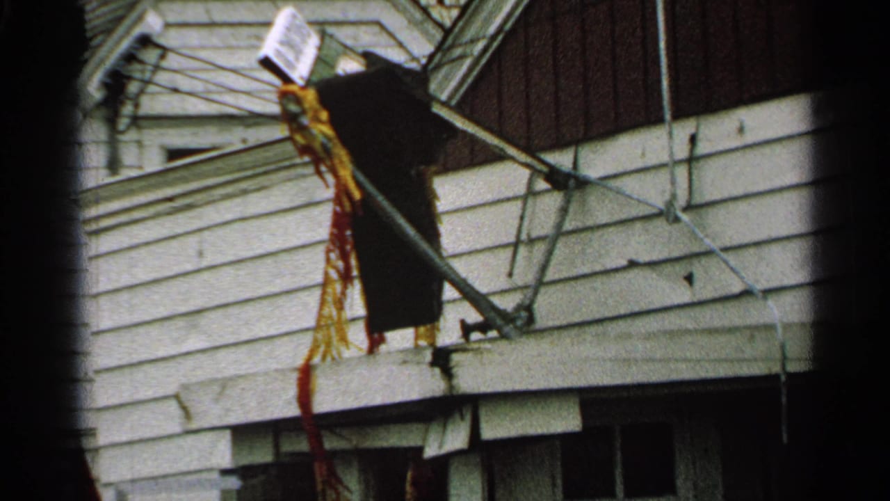 1965 Minnesota 8mm frame showing a broken antenna with hanging colored strips against residential siding.
