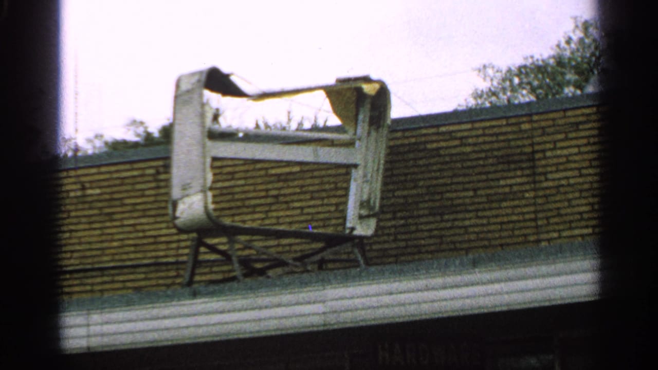1965 Minnesota 8mm frame showing a damaged TV-like shell or frame on a roof beside a brick wall.