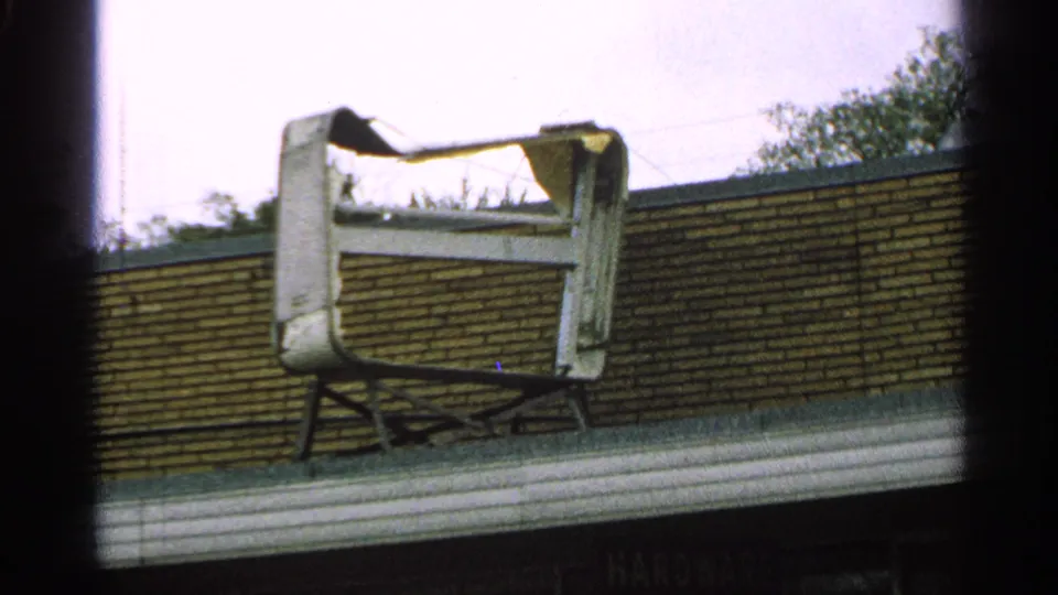 1965 Minnesota 8mm frame showing a damaged TV-like shell or frame on a roof beside a brick wall.