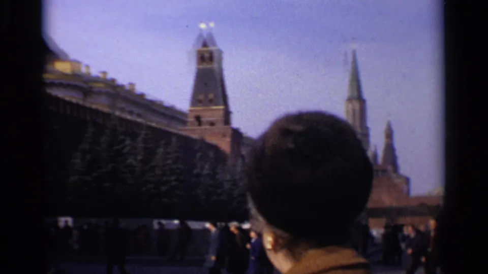 1965 Moscow home-movie frame showing the Kremlin wall and tower, with a foreground viewer partially blocking the scene.