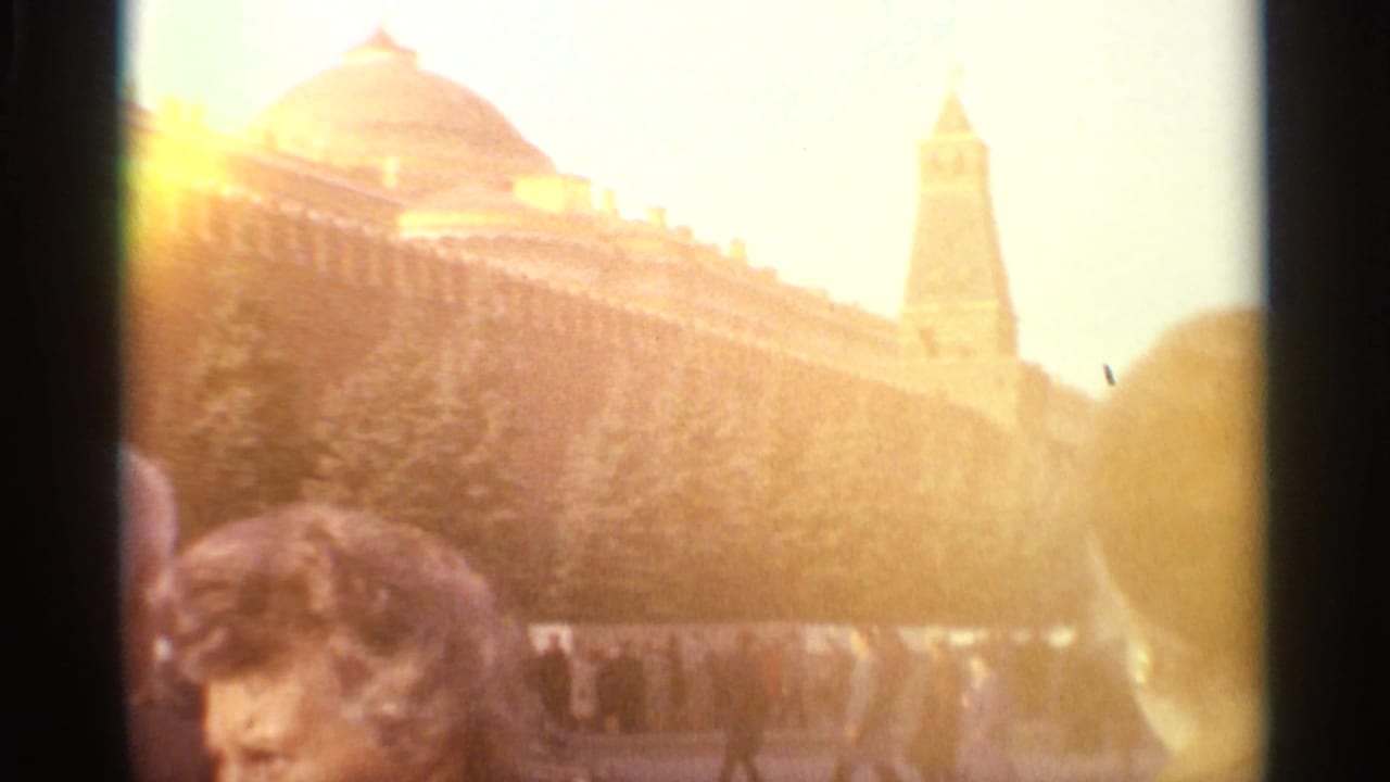 1965 Moscow home-movie frame showing visitors near Kremlin walls, golden domes and strong exposure flare.
