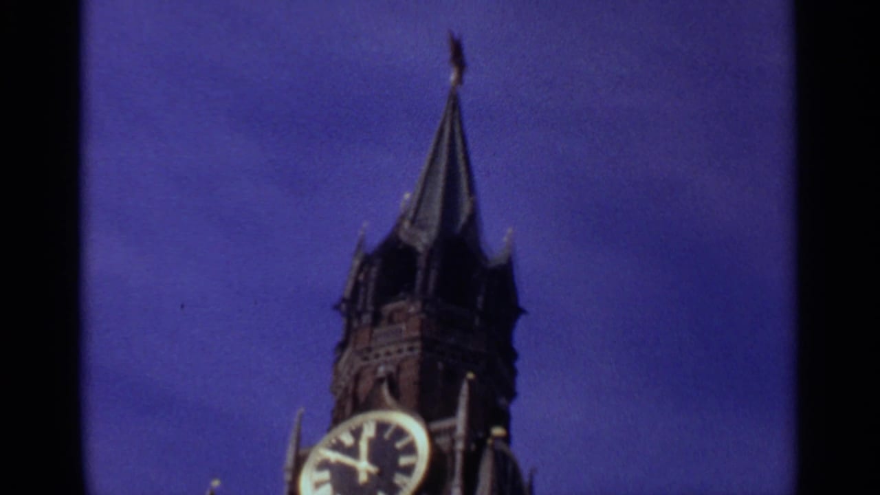 1965 Moscow home-movie frame showing the Spasskaya Tower clock face and tall spire, with dark film edges visible.