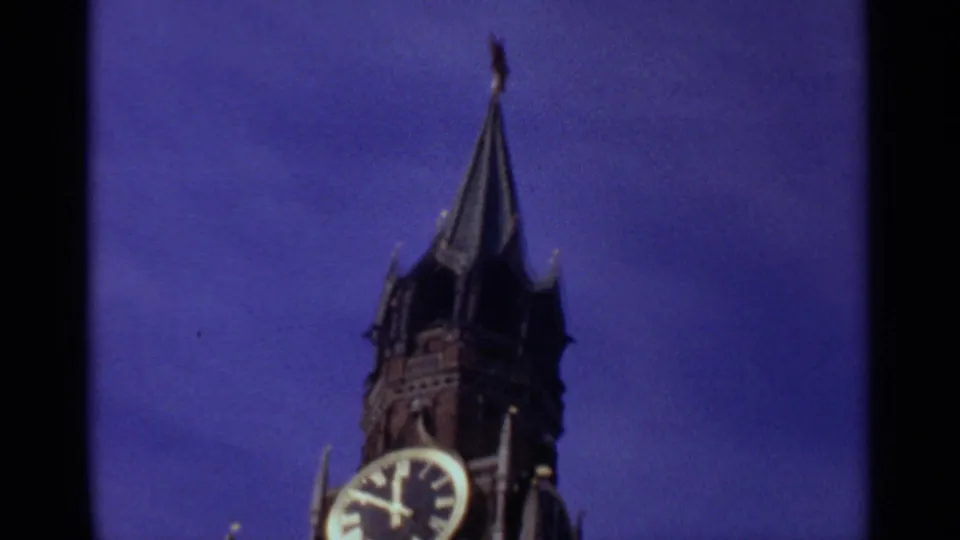 1965 Moscow home-movie frame showing the Spasskaya Tower clock face and tall spire, with dark film edges visible.