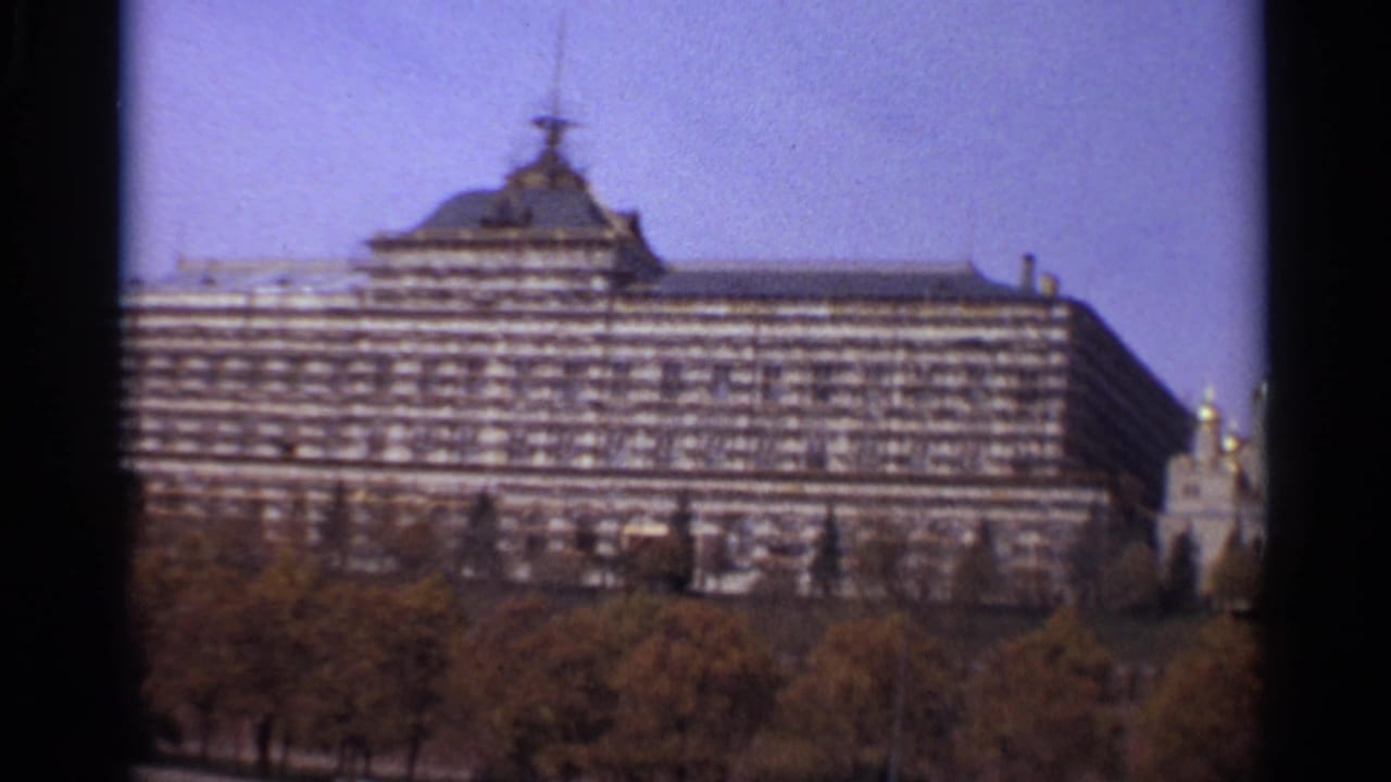 1965 Moscow frame showing the State Kremlin Palace facade above autumn trees, with a small domed church at the right edge.