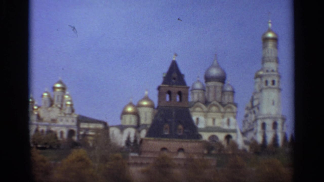 1965 Moscow 8mm frame showing Kremlin-area cathedral domes, a dark tower, a tall bell tower, trees, and pale blue sky.