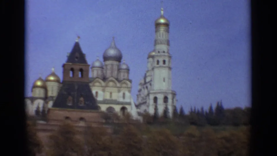 1965 Moscow home-movie frame with cathedral domes, a dark-roofed tower, the tall bell tower, and trees in the foreground.