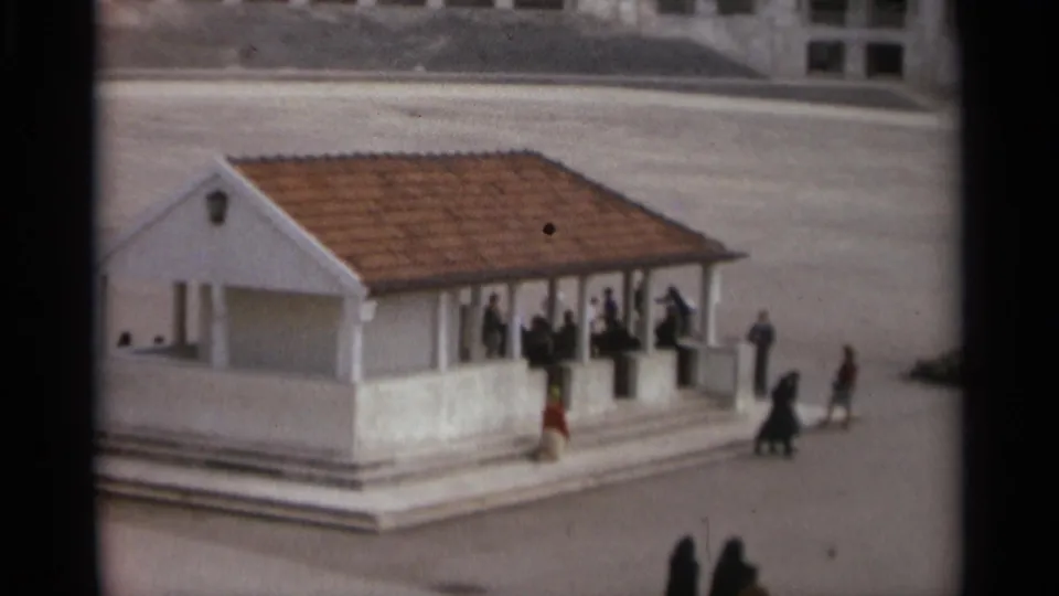 1965 Nazaré home-movie frame showing a small white pavilion with a terracotta roof and visitors gathered on its steps.