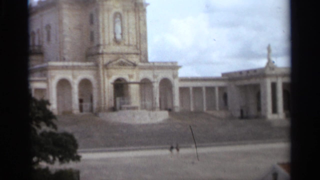 Basilica of Our Lady of Nazaré exterior in 1965, with arched facade, tower, colonnade, and distant visitors in the plaza.