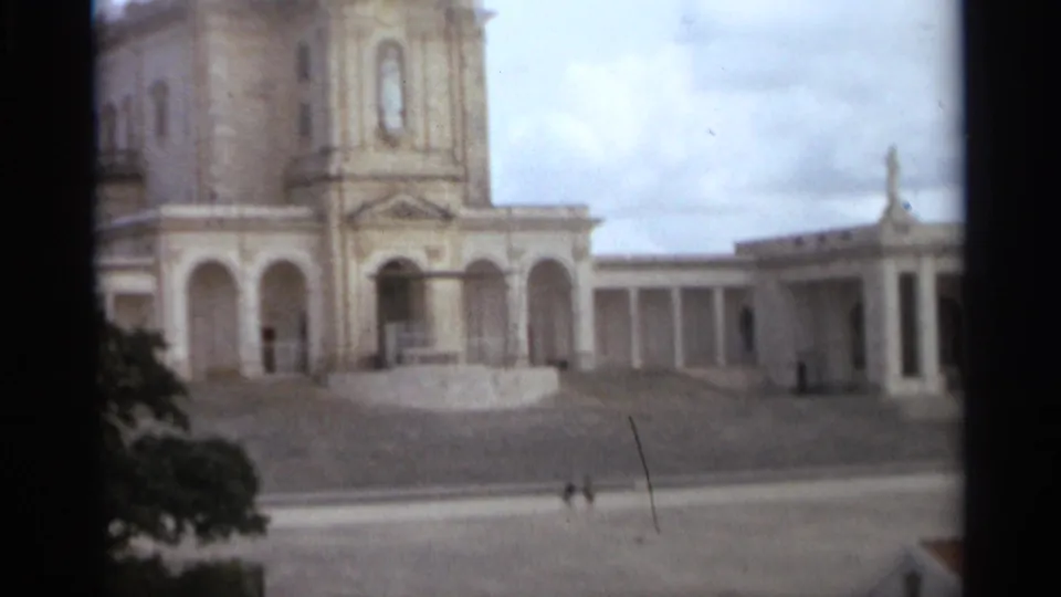 Basilica of Our Lady of Nazaré exterior in 1965, with arched facade, tower, colonnade, and distant visitors in the plaza.