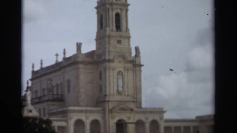 Side-angled 1965 view of the Basilica of Our Lady of Nazaré, showing its tower, ornate facade, roofline crosses, and cloudy sky.