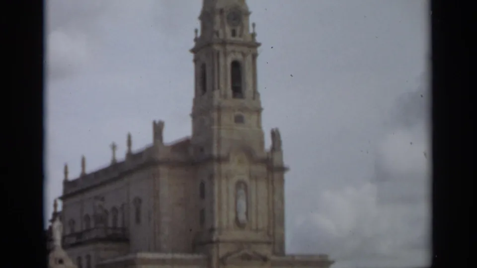1965 8mm frame from Nazaré, Portugal, showing an ornate church facade and tall bell tower in soft focus beneath an overcast sky.