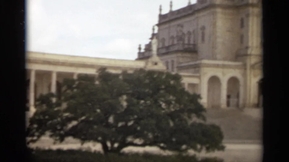 1965 Nazare, Portugal 8mm frame showing a grand arched building behind a large foreground tree.