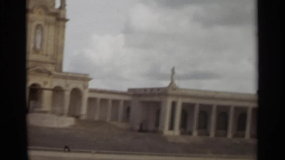 1965 Nazare home-movie frame showing a bell tower, columns, steps, and pale facade beneath a cloudy sky.