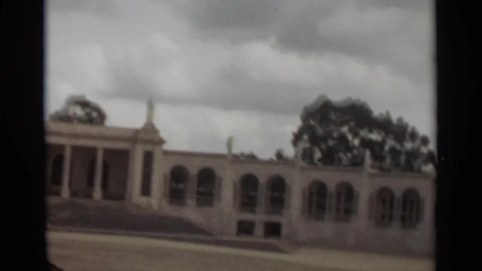 1965 Nazare home-movie view of an arched side facade, pale walls, steps, and trees beyond the roofline.