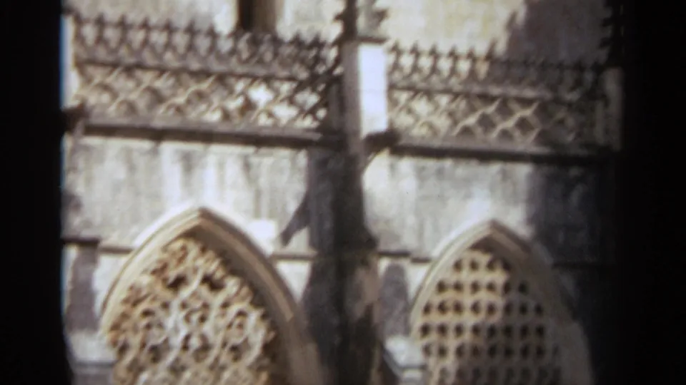 1965 Nazare, Portugal 8mm frame of a church cloister wall with pointed arched tracery, weathered stone blocks, and vertical shadow.