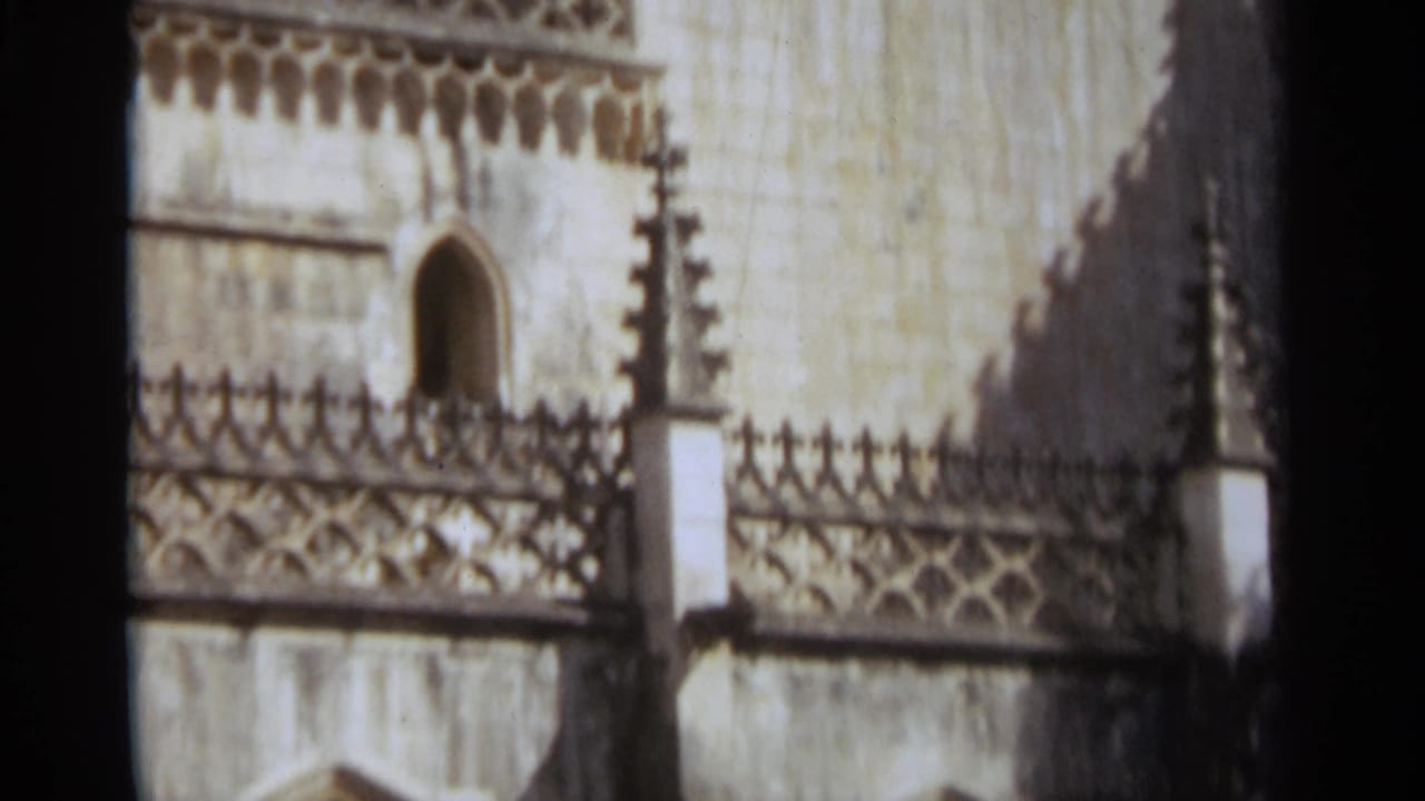 Close view of a pale stone church tower with pointed arch opening and carved parapet.