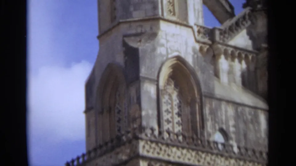 1965 Nazaré, Portugal 8mm frame showing a church facade section with arched window recess, carved ornament, parapet, and sky.
