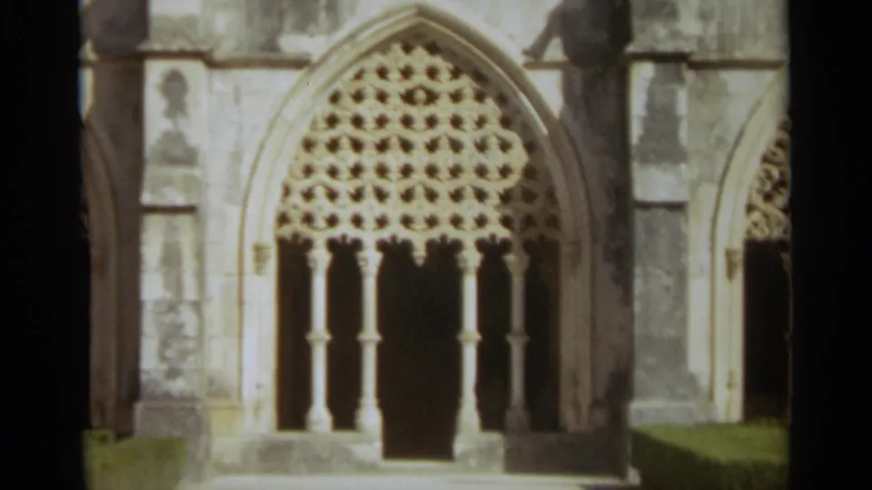 Close visitor-shot view of a Gothic-style arched church window in Nazaré, Portugal, with lattice-like stonework and deep shadowed openings.