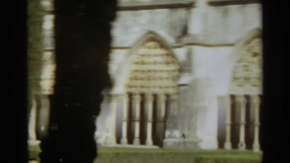 Soft 8mm frame of the Nazaré church facade, with arched windows, pale masonry and a dark vertical tree or shadow crossing the view.