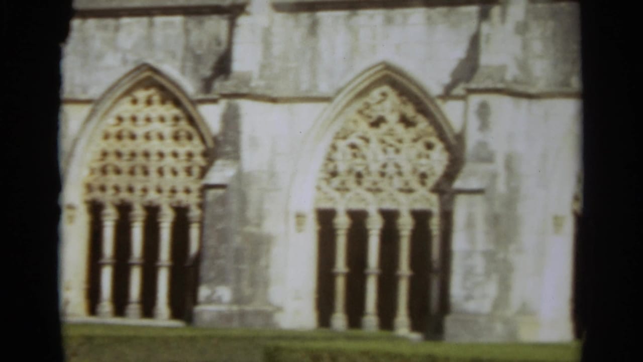 1965 Nazaré, Portugal 8mm frame showing ornate pointed church windows, carved stone tracery, and weathered masonry.