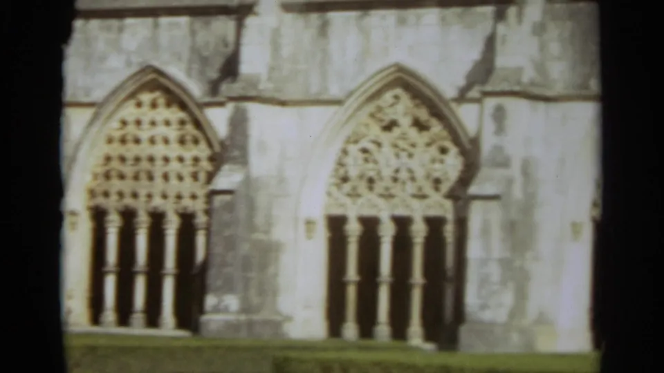 1965 Nazaré, Portugal 8mm frame showing ornate pointed church windows, carved stone tracery, and weathered masonry.