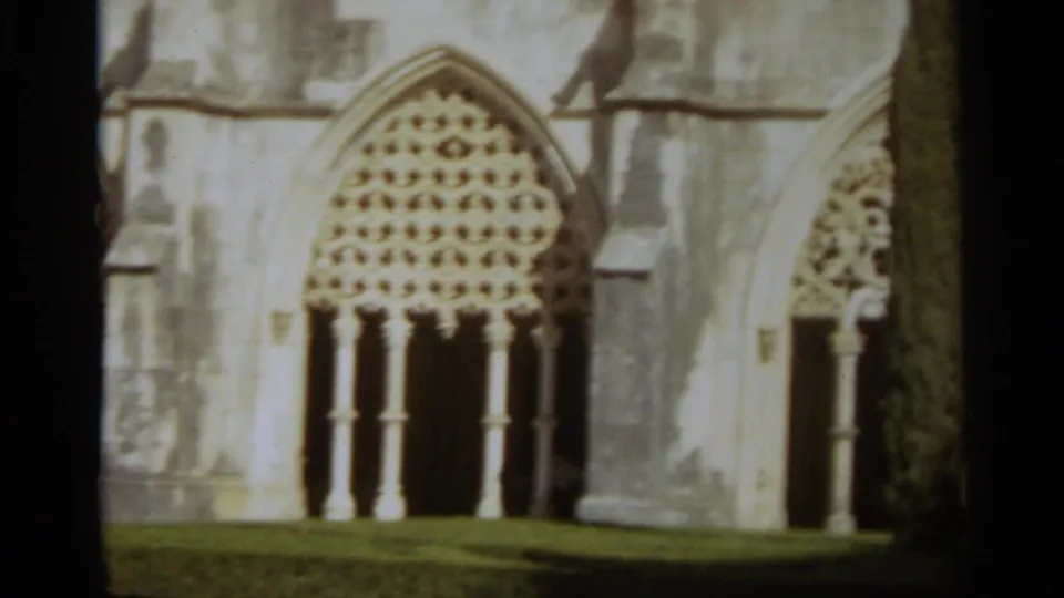 Visitor-shot 8mm view of a pale stone church facade in Nazaré, Portugal, centered on a large arched traceried window.